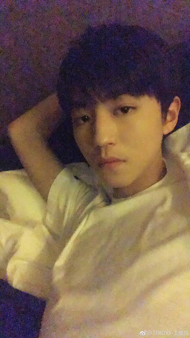 照片中,王俊凯身穿白色短袖,一只手当枕头,慵懒的躺在床上,表情酷帅