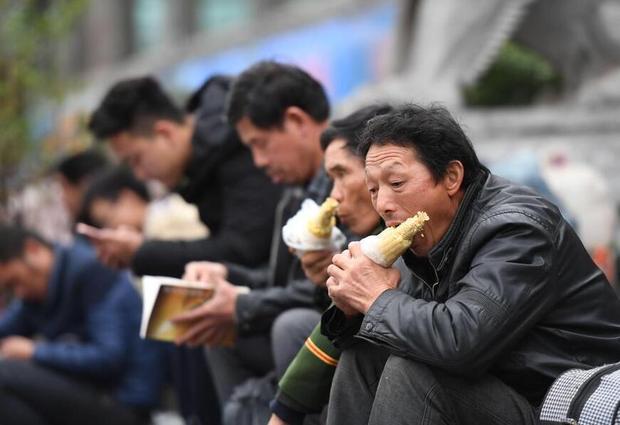 2017年1月22日，广西南宁的火车站，挤满了买票、候车的人潮。广场上搭建的临时候车室里面，南来北往的旅客在这里聚集，这里也成了各式各样的“午餐”聚会处。很多旅客拿出行李中的食物有滋有味地吃起来，候车厅中弥漫着各种食物的味道。每年春运，陪伴人们返乡的，除了必要的行李和给老人、孩子的礼物外，就是旅途中的食物了。图为广场上两位大叔正在啃着香喷喷的玉米棒子。