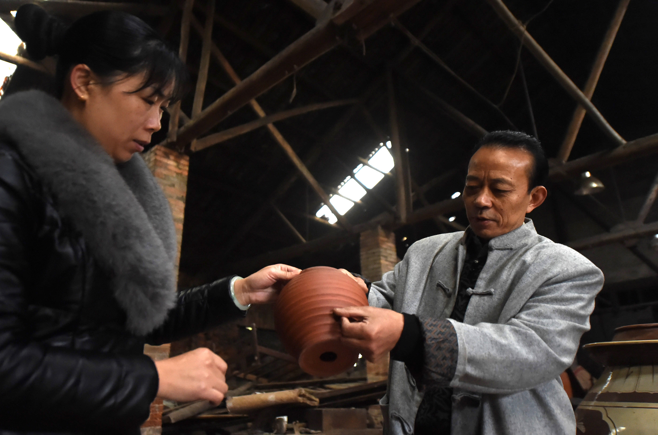 12月14日,梁先才在自己的手工制陶车间展示一个刻有荣昌陶制作