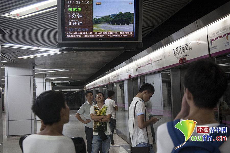 北京市民在地铁5号线惠新西街南口站内观看阅兵式直播